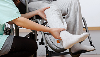 A physical therapist or nurse assisting a person in a wheelchair by supporting their leg representing personal injury
